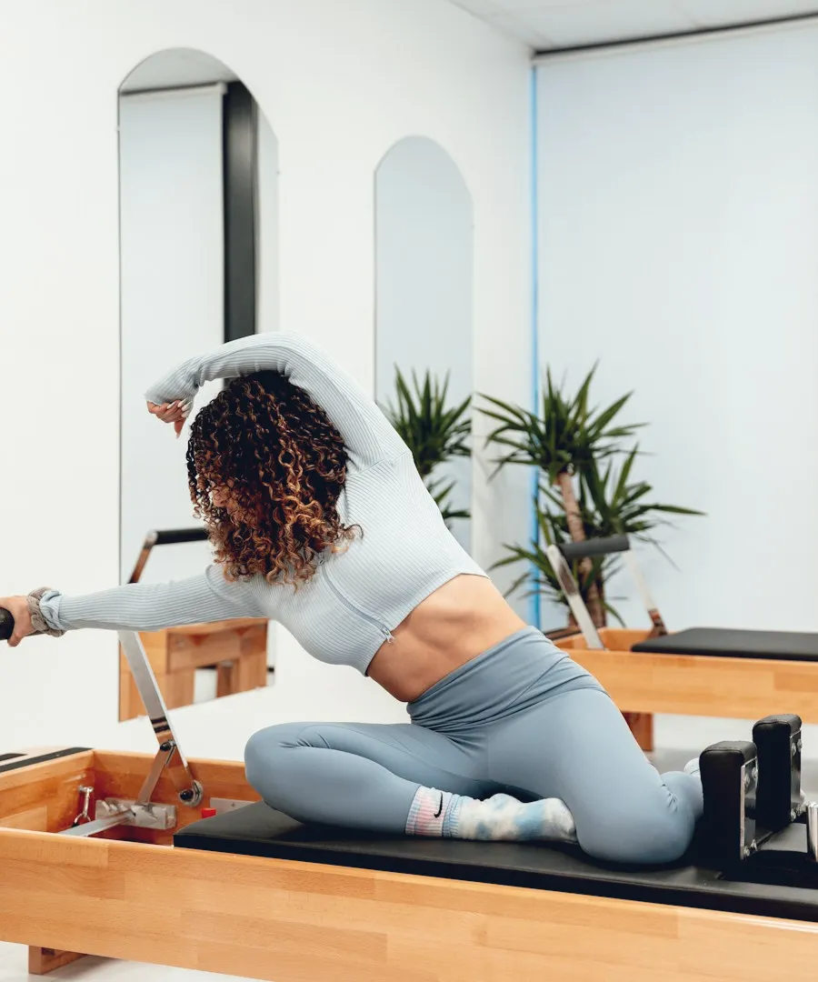 Woman stretching on a reformer in a bright Pilates studio
