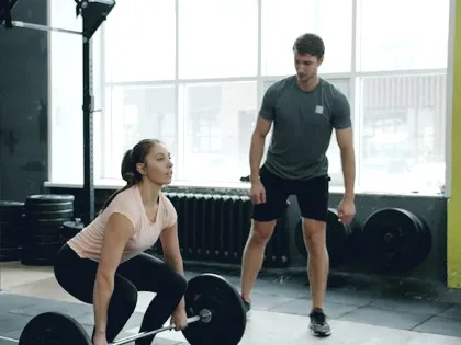 Personal trainer coaching a client with a barbell