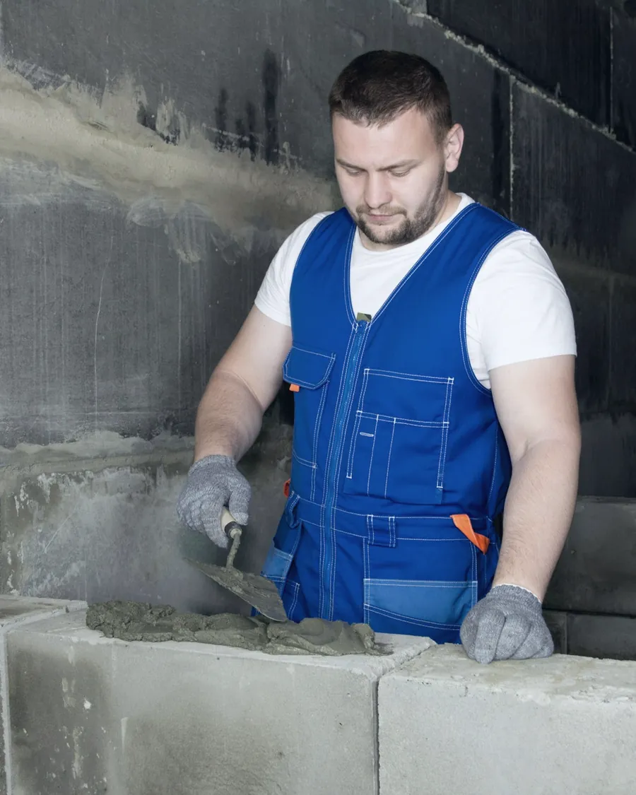 Maçon en gilet de travail qui monte un mur